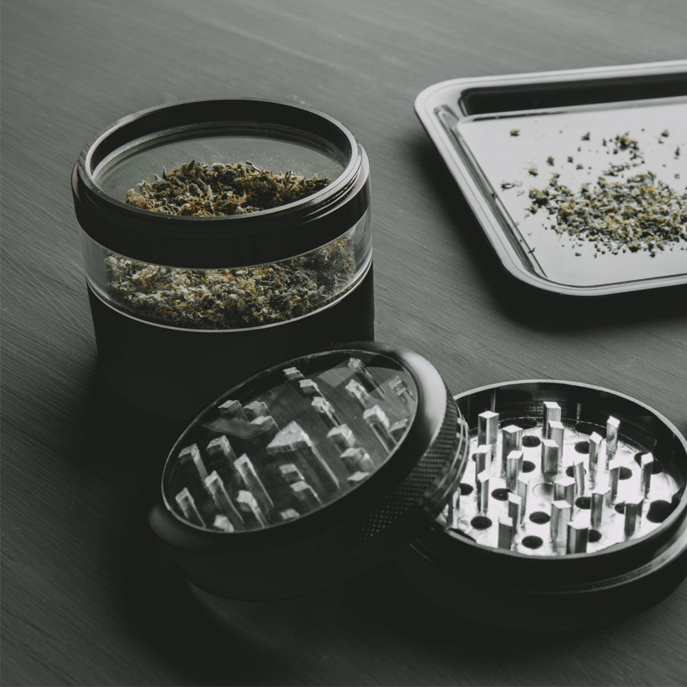 Herb grinder with cannabis bud in it and tray with ground herbs in the background