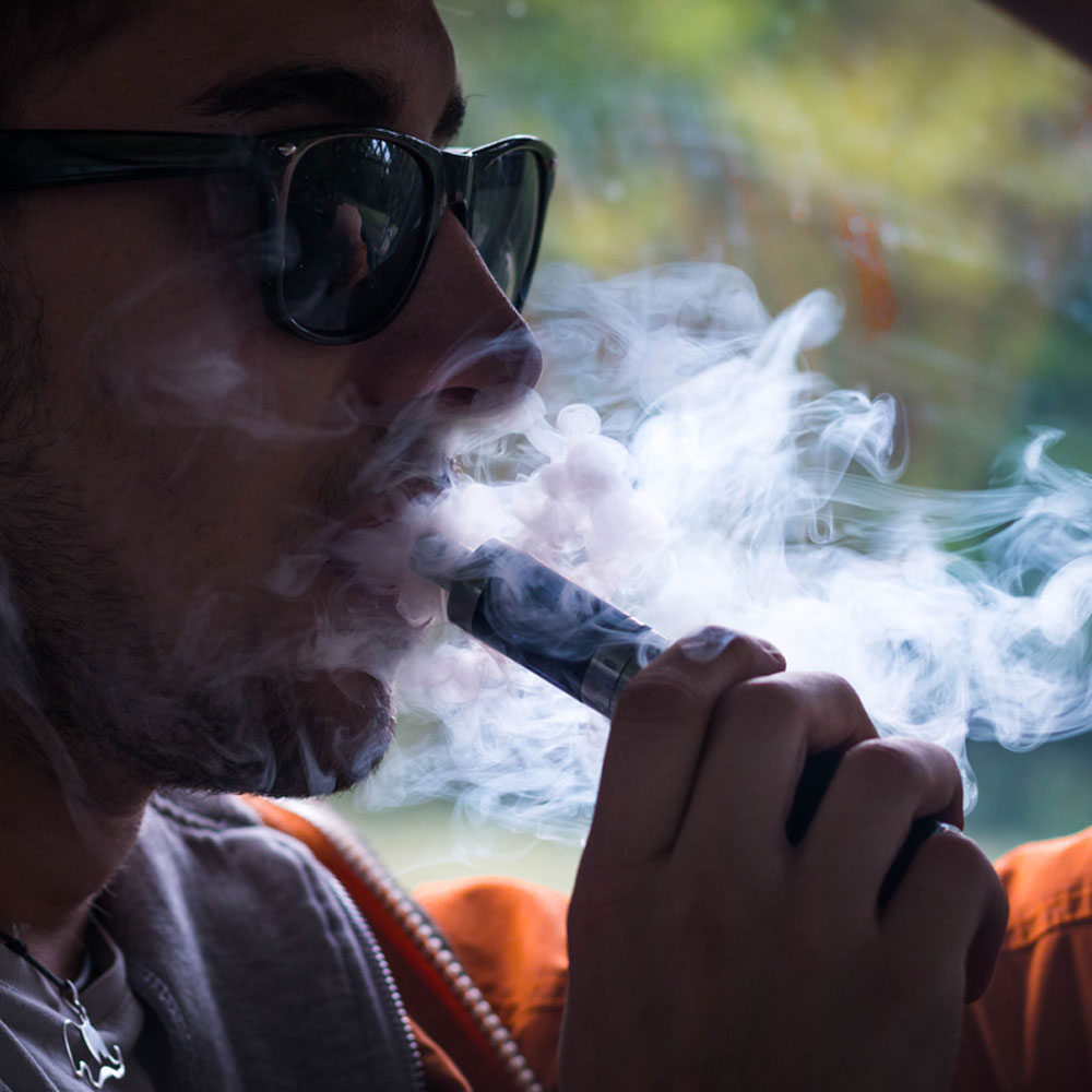 A man vaping and blowing out smoke inside a car