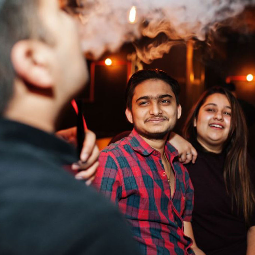 A man vaping and two friends smiling at him