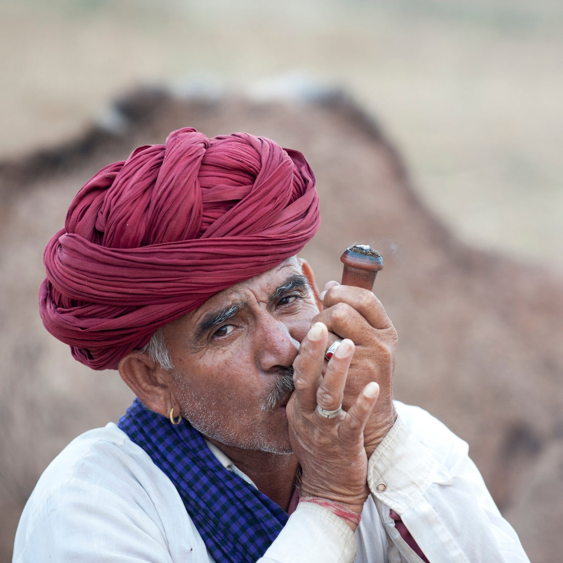 Man in red headdress smoking a wooden chillum pipe